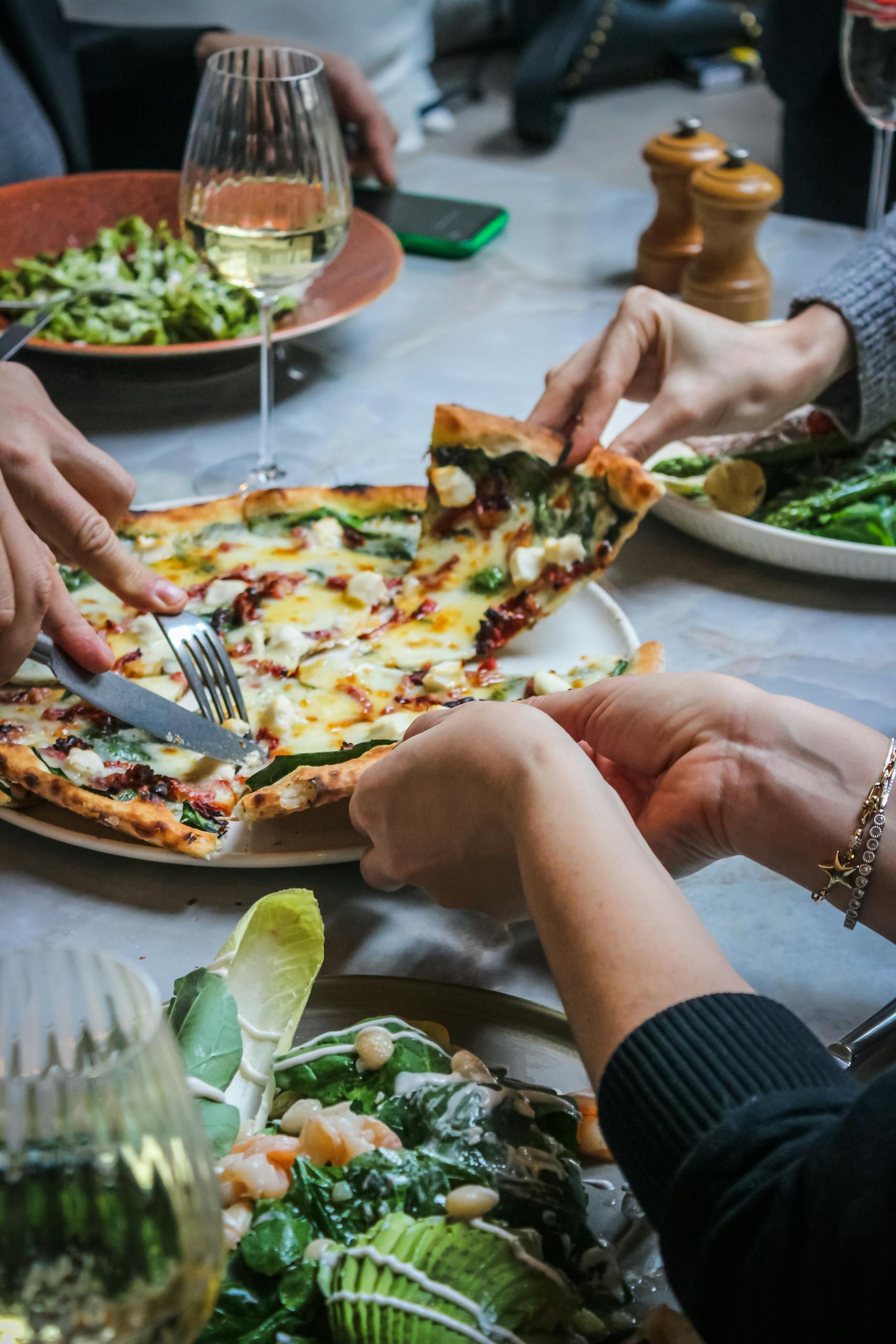 Hands around Pizza on Table