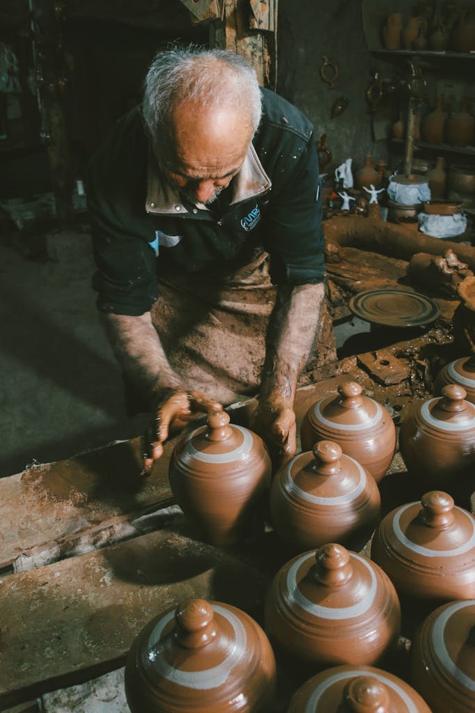 Senior potter shaping clay jugs in a rustic workshop setting, showcasing craftsmanship.