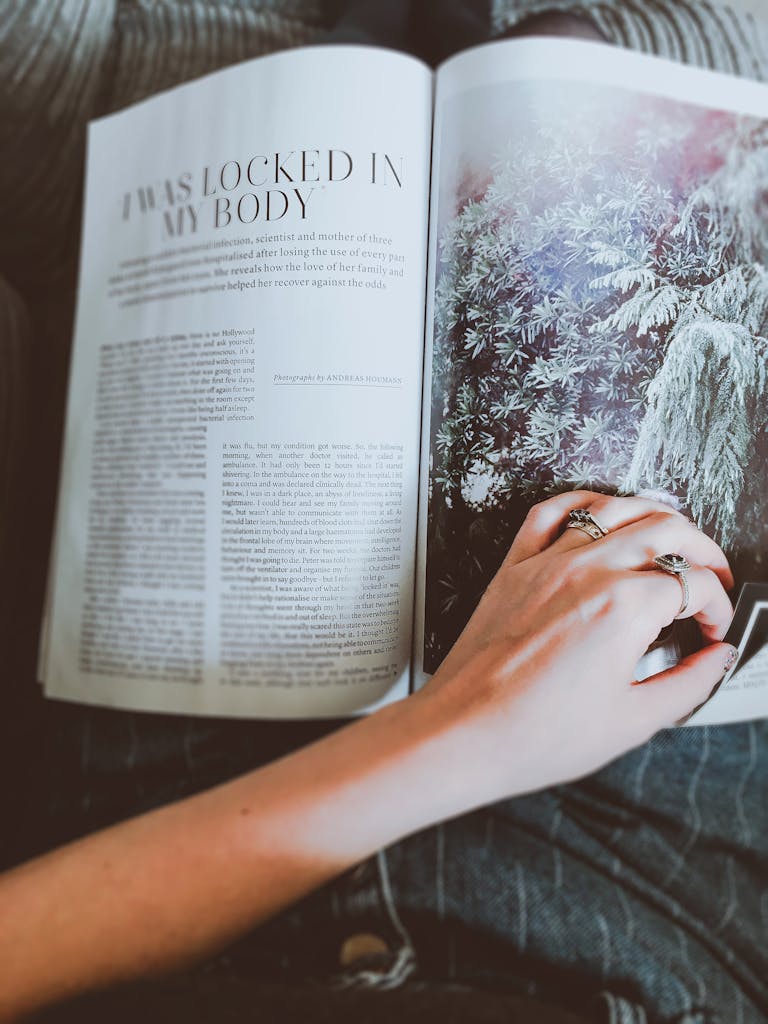 A person leisurely reading a magazine, showcasing a hand with rings on vibrant pages.