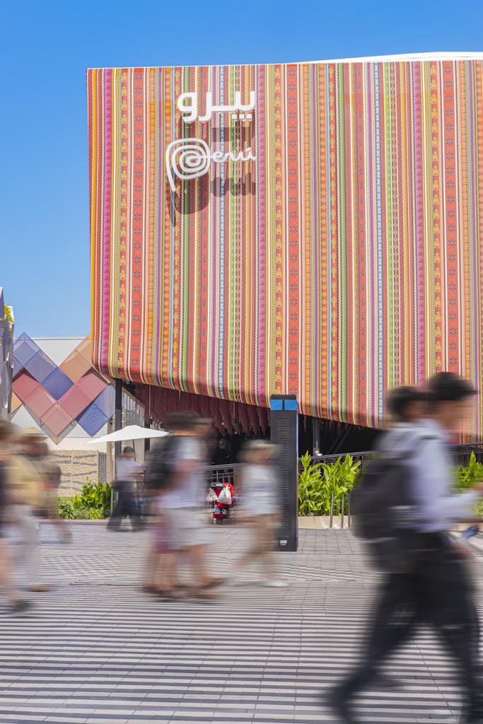 Blurred visitors walking past a colorful pavilion facade at Dubai Expo 2020.