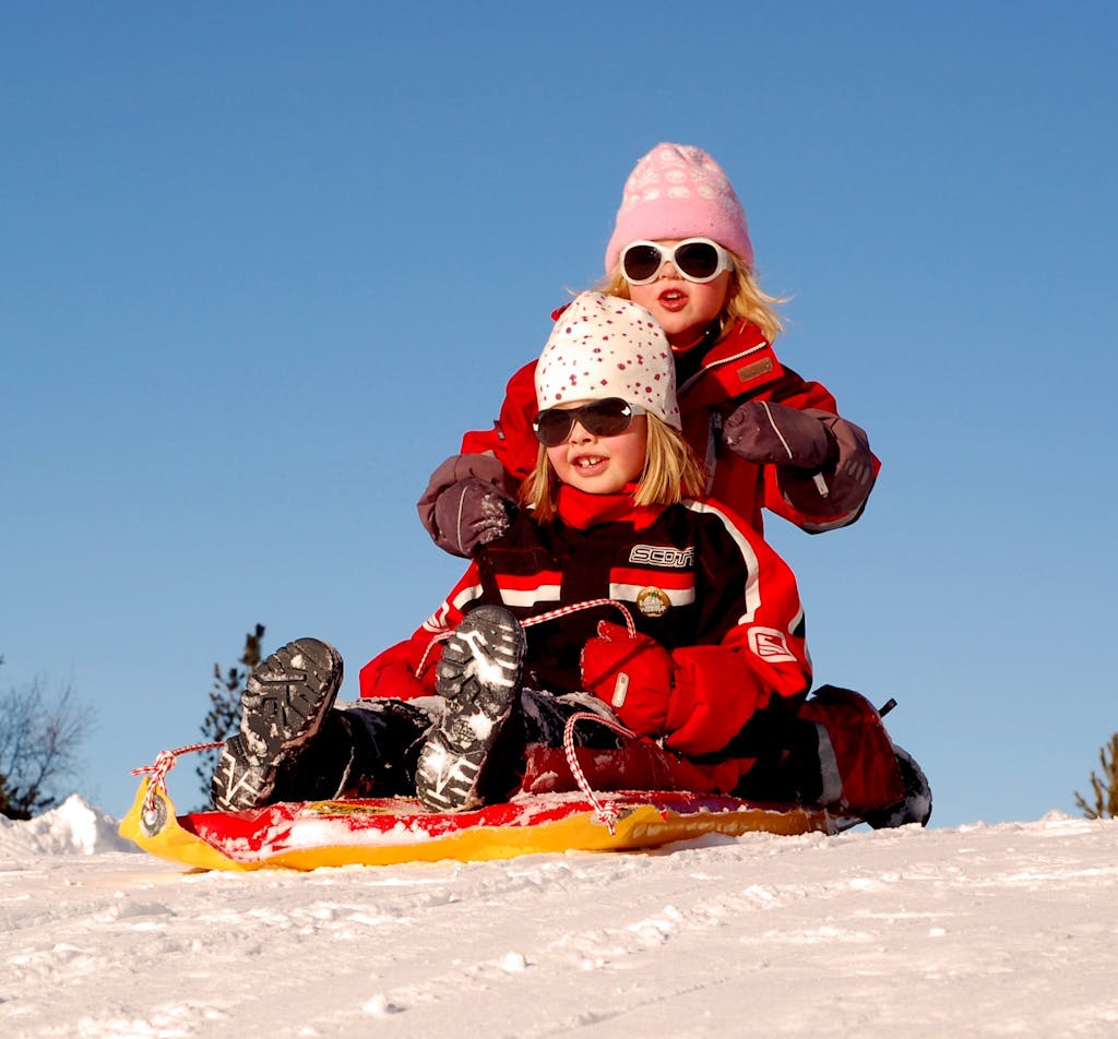 Two children enjoying a fun sled ride down a snowy hill on a sunny winter day.